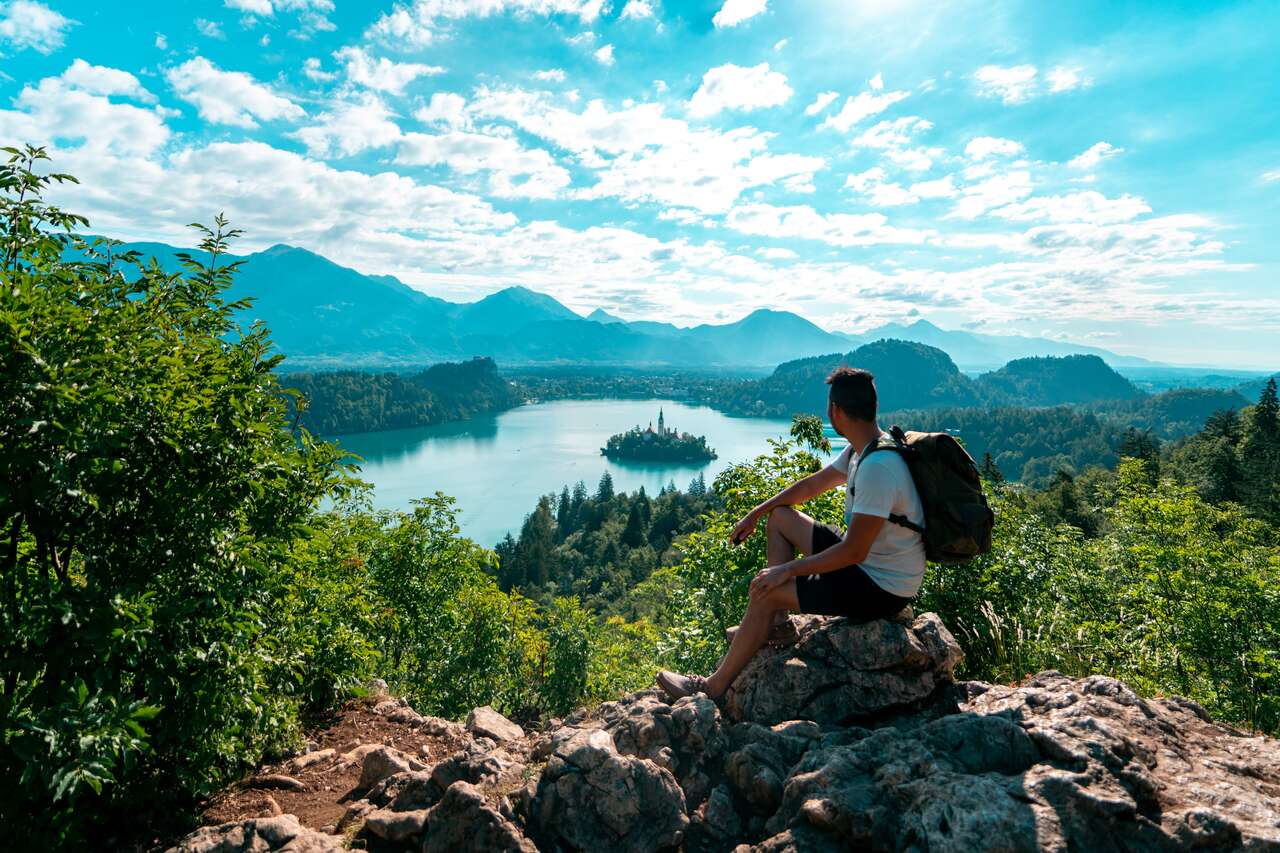 A person sitting on a rock looking at Lake Bled from Ojstrica